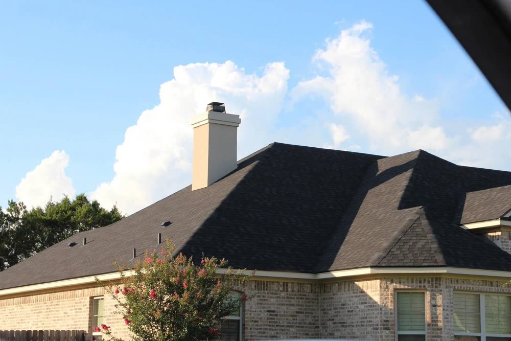 A dark shingle roof with a white brick chimney under a blue sky
