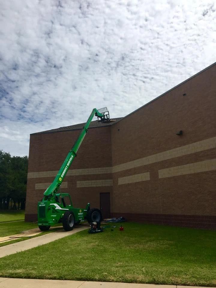 A green lift parked beside a brick commercial building during a roofing job