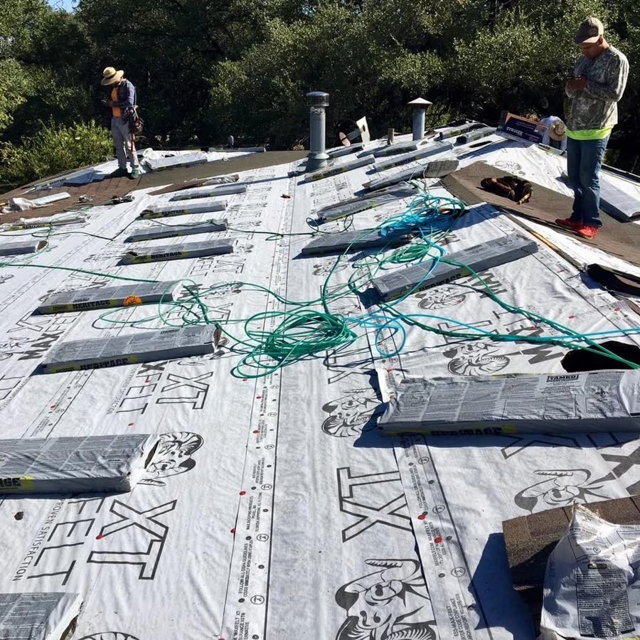 Two roofers on a roof covered in synthetic felt, with vents and cables laid out