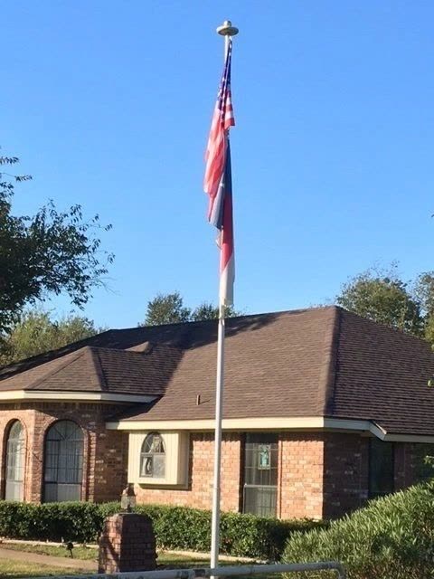 A brick home with a shingle roof and a flagpole in the yard
