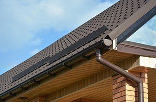 A brown gutter and downspout under a metal roof edge