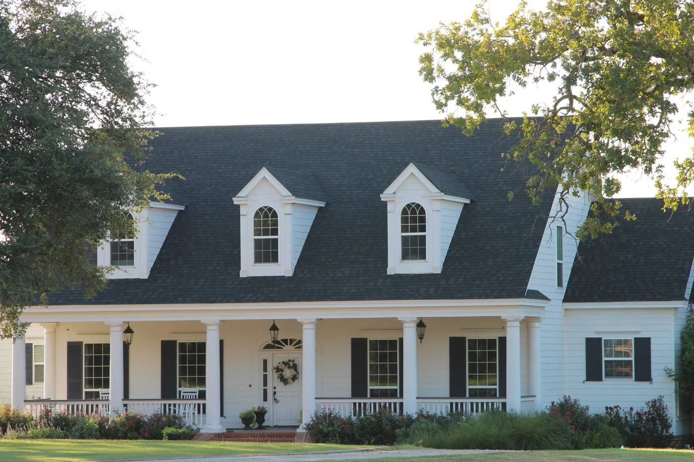 A white two-story house with dormers and a finished dark shingle roof
